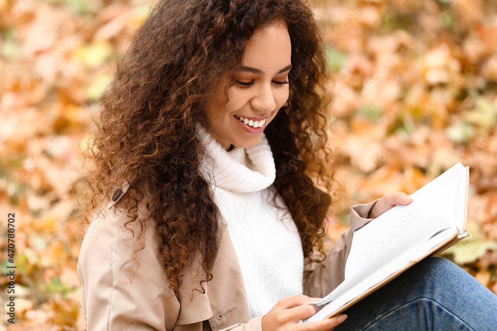 微笑的非裔美国妇女在秋季公园读书