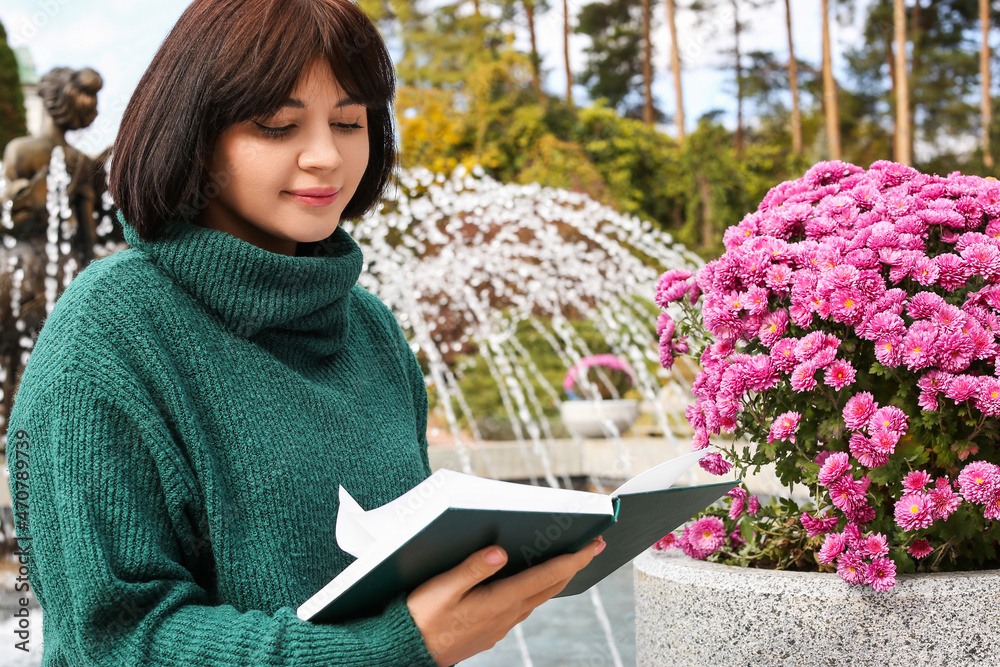 年轻女子在秋天公园里鲜花盛开的花坛旁看书