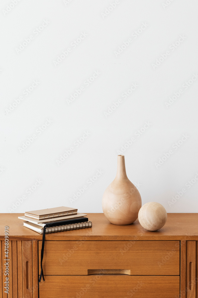 白色房间的木制橱柜上的木制花瓶旁的一摞笔记本