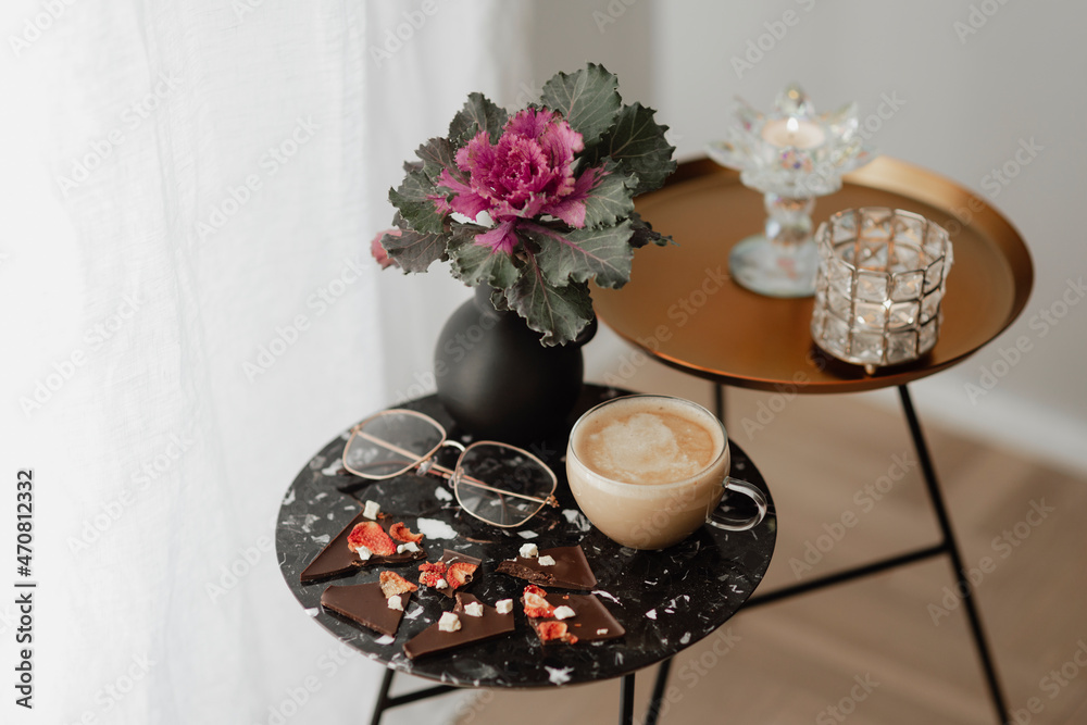 一杯奶茶和眼镜放在窗帘旁边的黑色桌子上