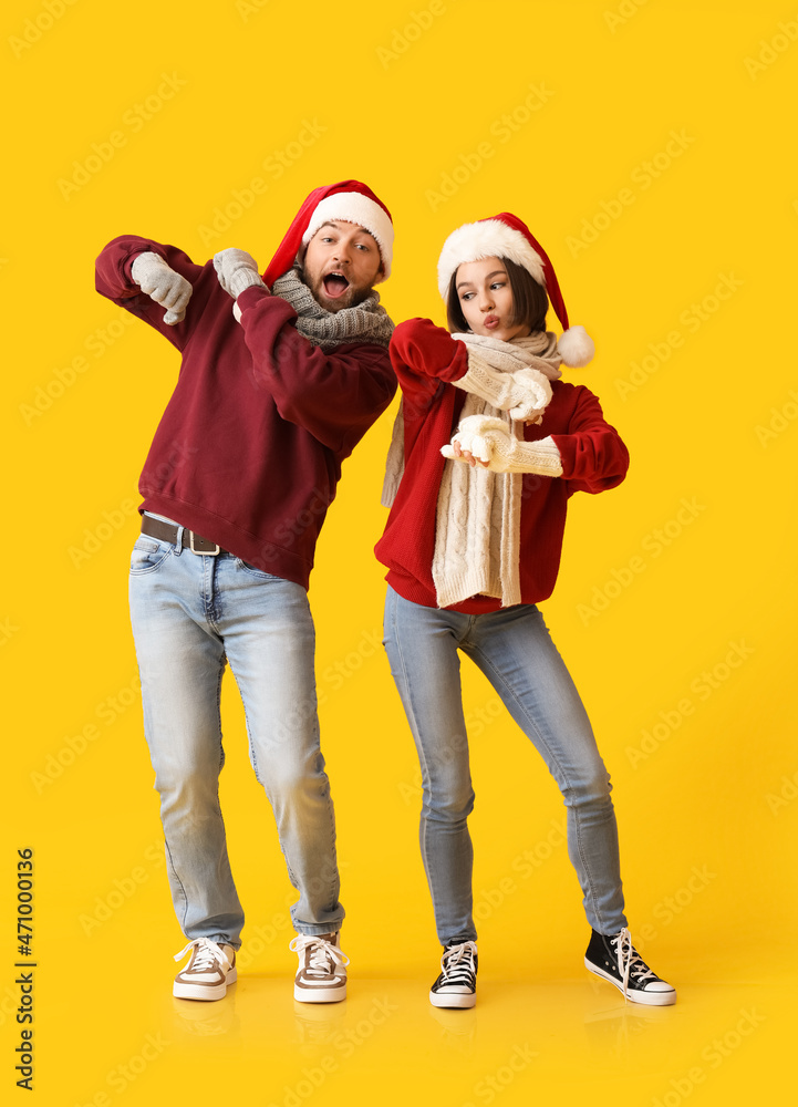 跳舞的年轻情侣穿着时尚的冬装，戴着彩色背景的圣诞老人帽
