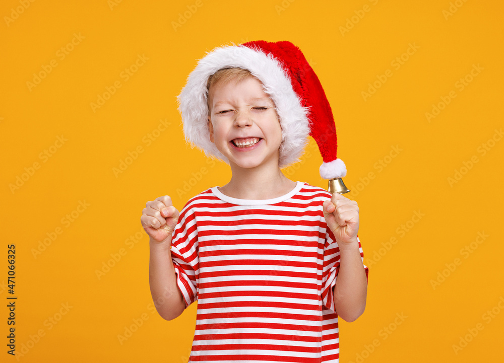 快乐的小男孩戴着圣诞老人帽，闭着眼睛，紧握拳头，许下圣诞愿望