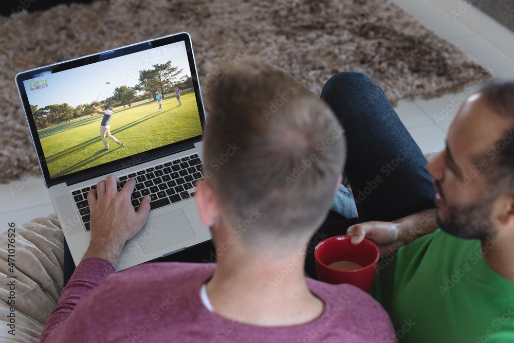 两个不同的男性朋友在家用笔记本电脑看高尔夫比赛