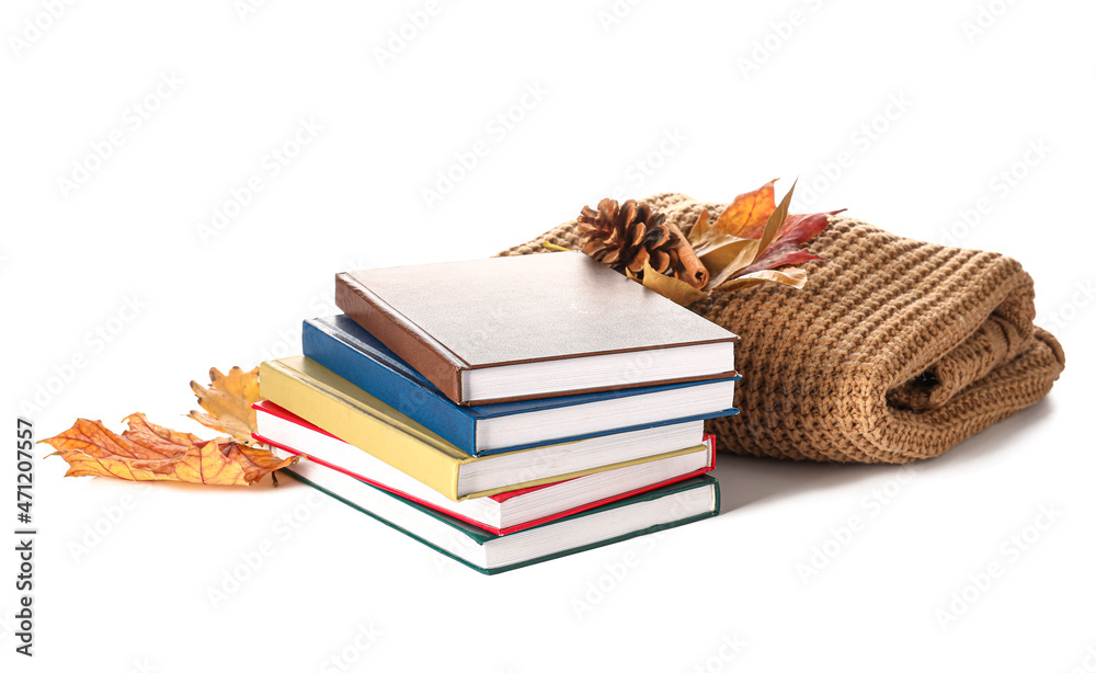 白色背景上堆叠着不同的书籍、针织毛衣和秋季装饰