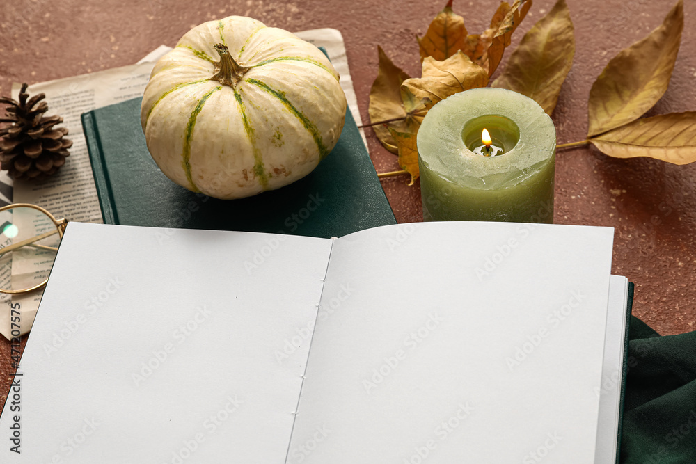 打开的书上有空白页、南瓜、燃烧的蜡烛和彩色桌子上的秋季装饰