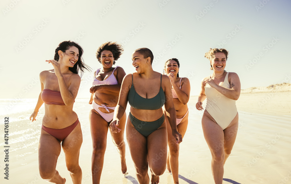 快乐的年轻女性穿着比基尼在海滩上跑步
