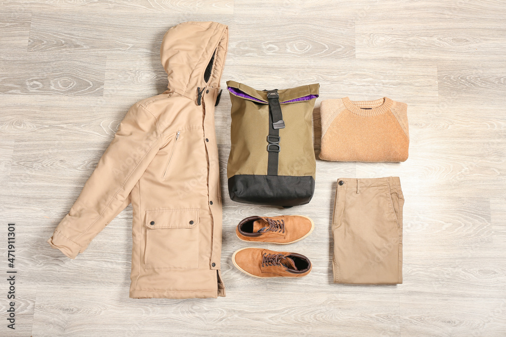 浅色木质背景的时尚男性夹克、背包、鞋子、毛衣和裤子