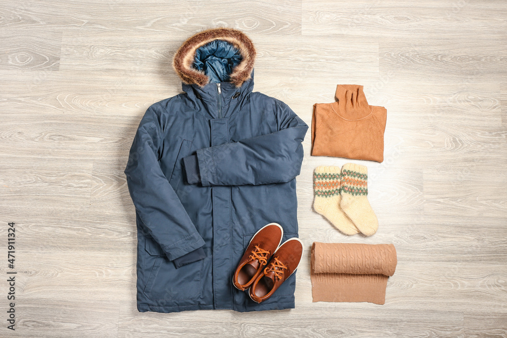 浅色木质背景的冬季夹克、毛衣、袜子、围巾和鞋子