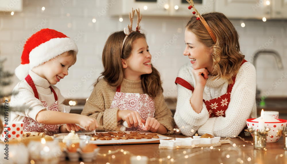 快乐的家庭母亲和两个穿着节日服装的孩子一起在厨房做圣诞饼干