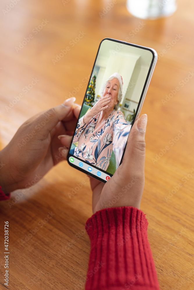 Hands of woman making christmas smartphone video call with senior caucasian woman blowing kiss