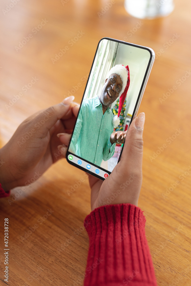 与戴圣诞老人帽的非洲裔美国老人进行圣诞智能手机视频通话的女人的手