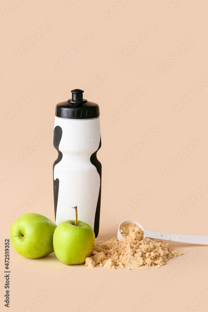 Bottle with protein shake, measuring scoop with powder and apples on color background