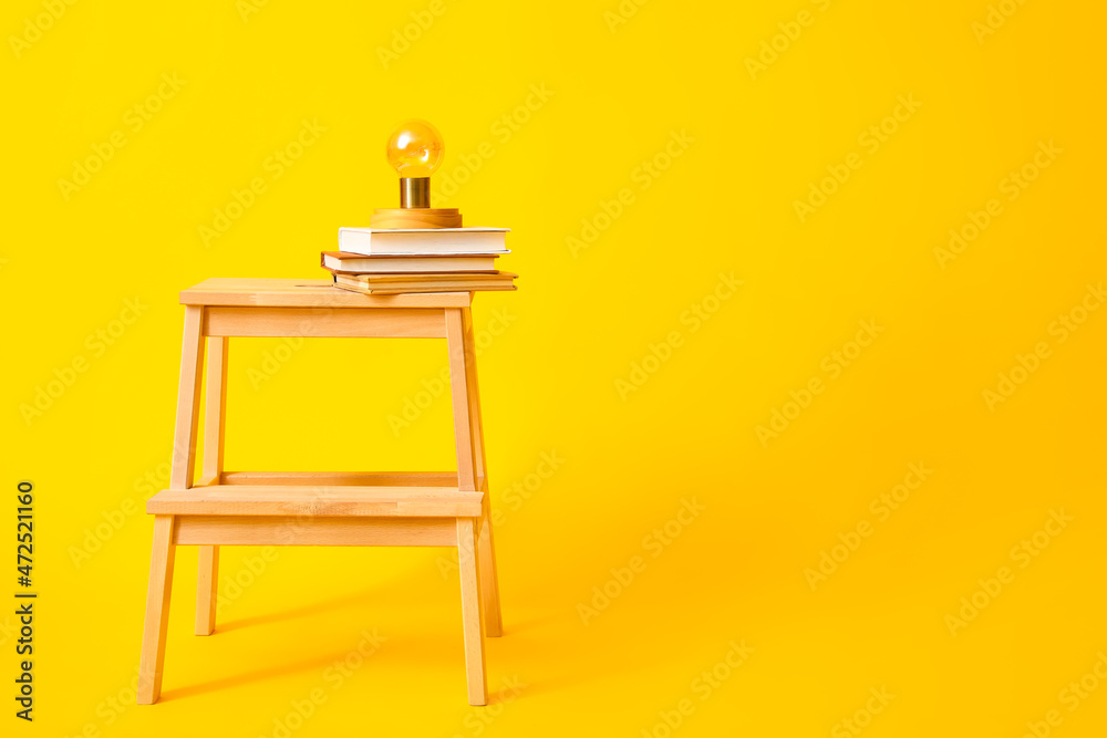 黄色背景上有书和灯的木制台阶凳
