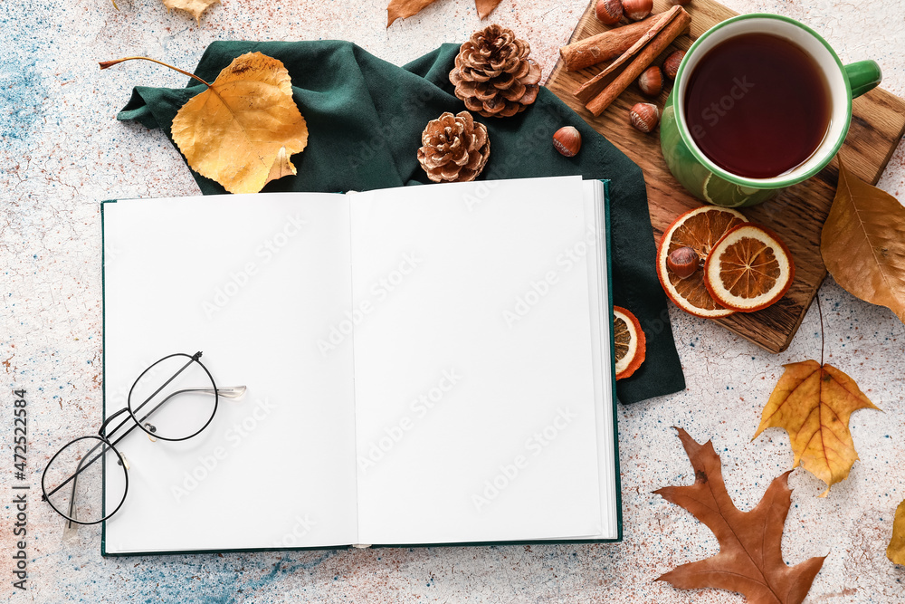 Opened book with blank pages, eyeglasses, cup of tea and autumn decor on light background