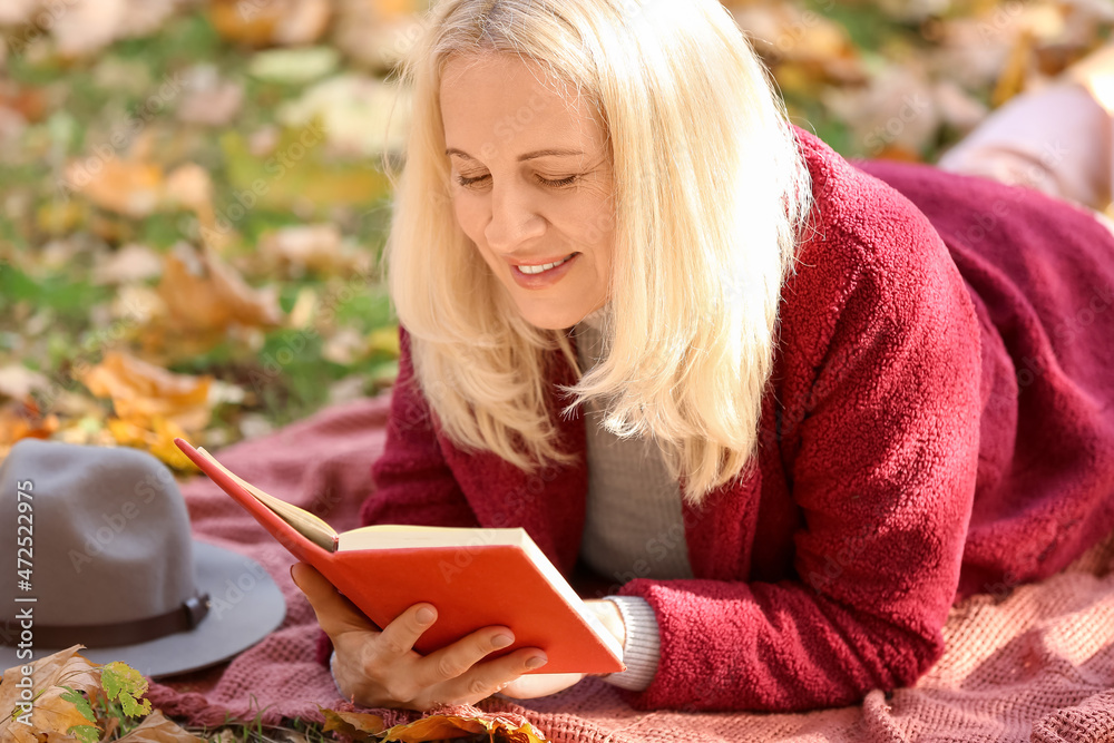 成熟的女人在秋季公园看书