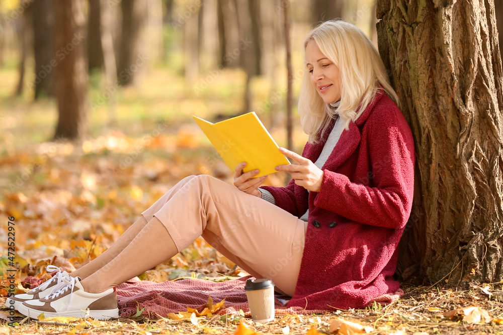 成熟女人在秋季公园读书