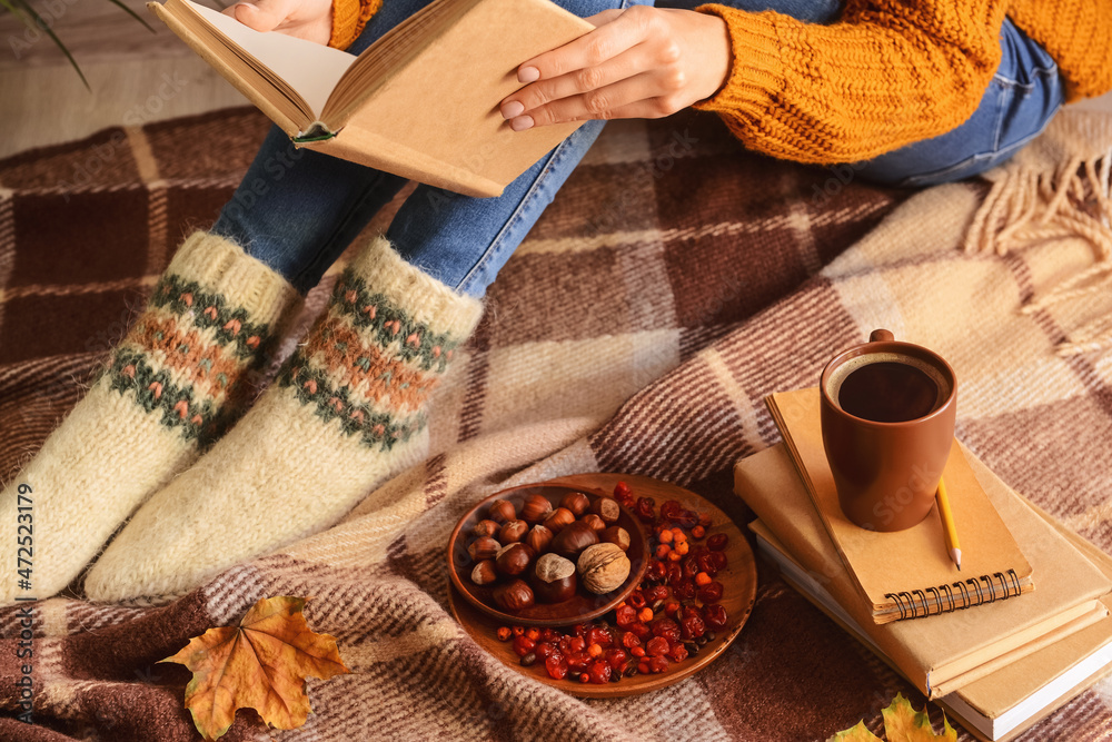 穿着保暖袜子的女人，格子布背景上有书、一杯咖啡、食物和秋叶