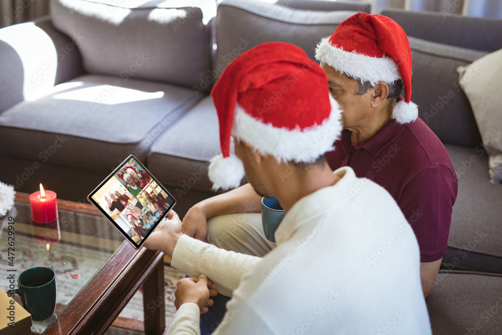 戴着圣诞老人帽的混血父亲和成年儿子与朋友进行平板电脑圣诞群视频通话