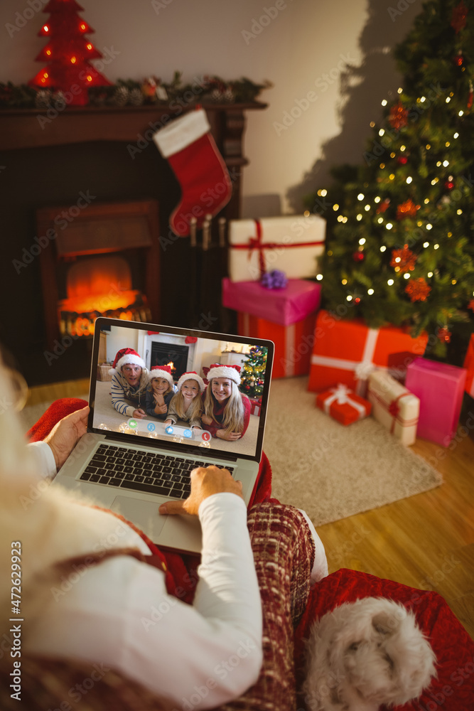 圣诞老人与戴着圣诞老人帽微笑的高加索家庭进行笔记本电脑圣诞视频通话