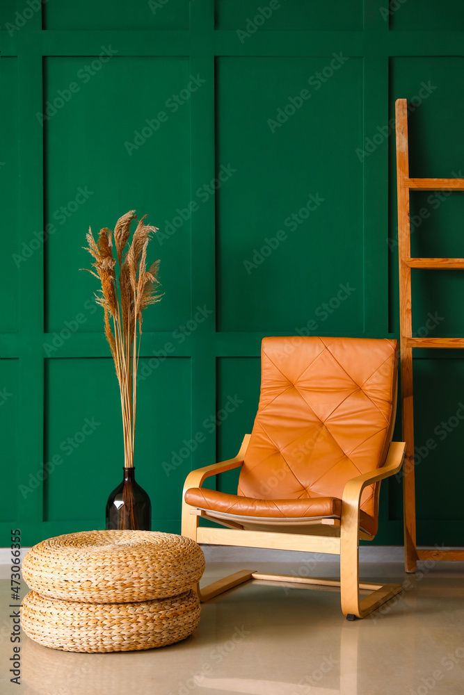 绿色墙壁附近带有干芦苇、扶手椅、梯子和袋的花瓶
