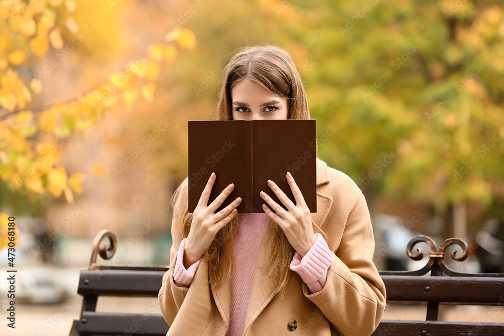 秋天公园长椅上拿着书的年轻女子