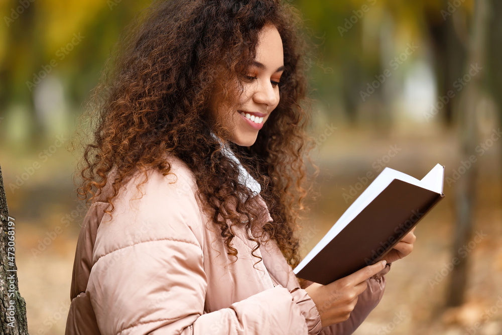 美丽微笑的非裔美国妇女在秋季公园看书