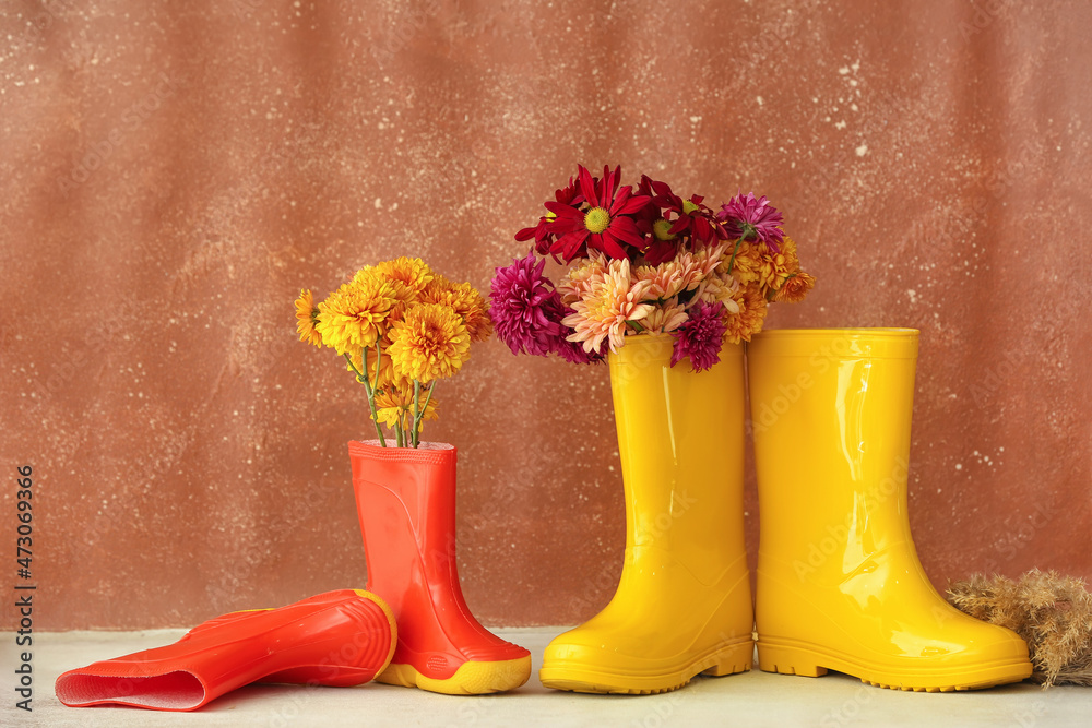 Rubber boots and autumn flowers against color wall
