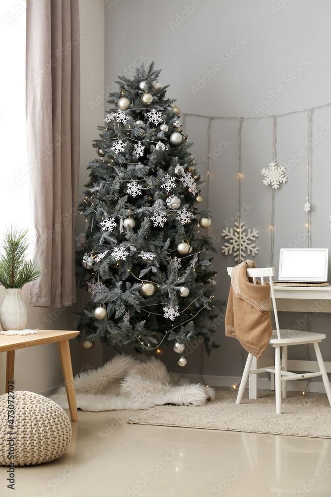Christmas tree and workplace with modern laptop near grey wall in room