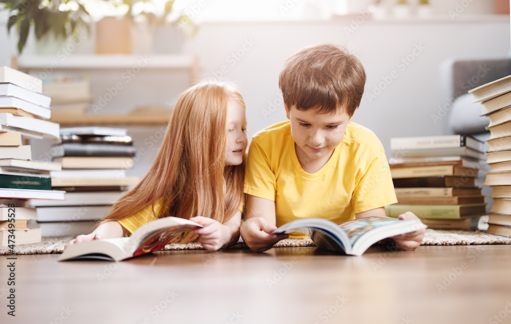 两个可爱的孩子躺在室内地板上，头上顶着书