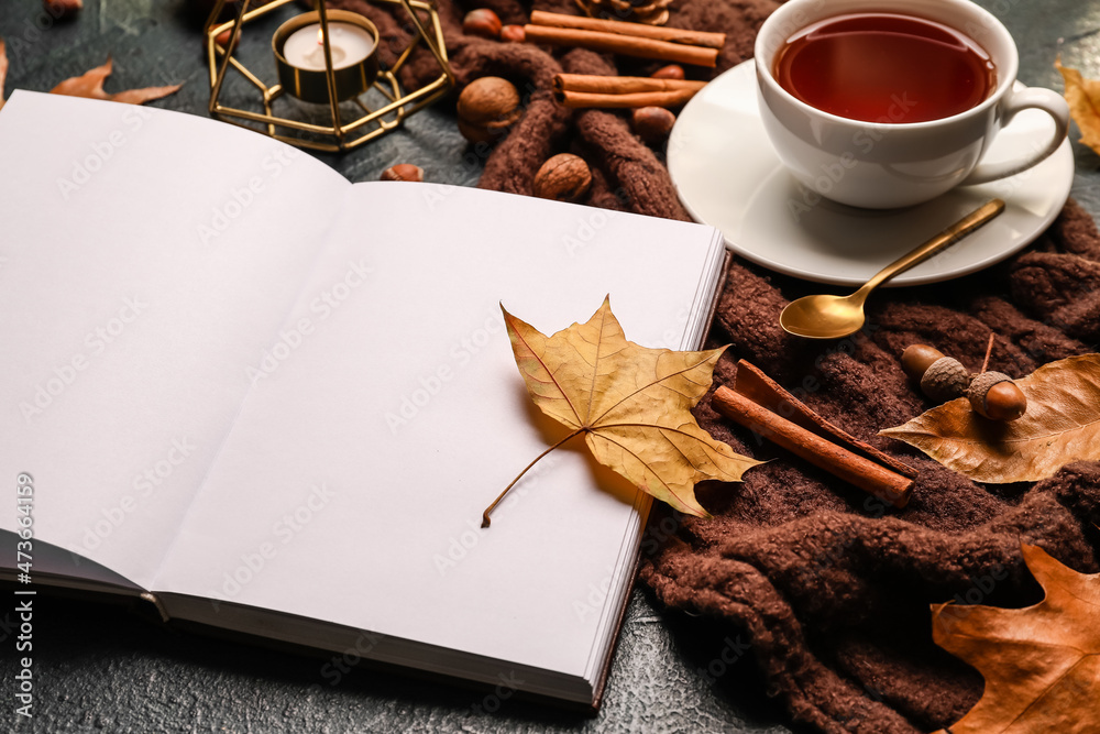 打开的书、蜡烛、一杯茶和深色桌子上的秋季装饰