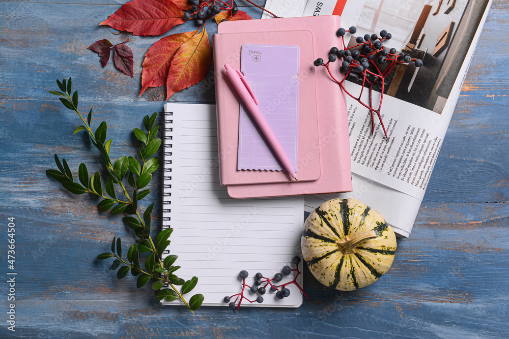 蓝色木质背景上有钢笔、报纸和秋季装饰的笔记本