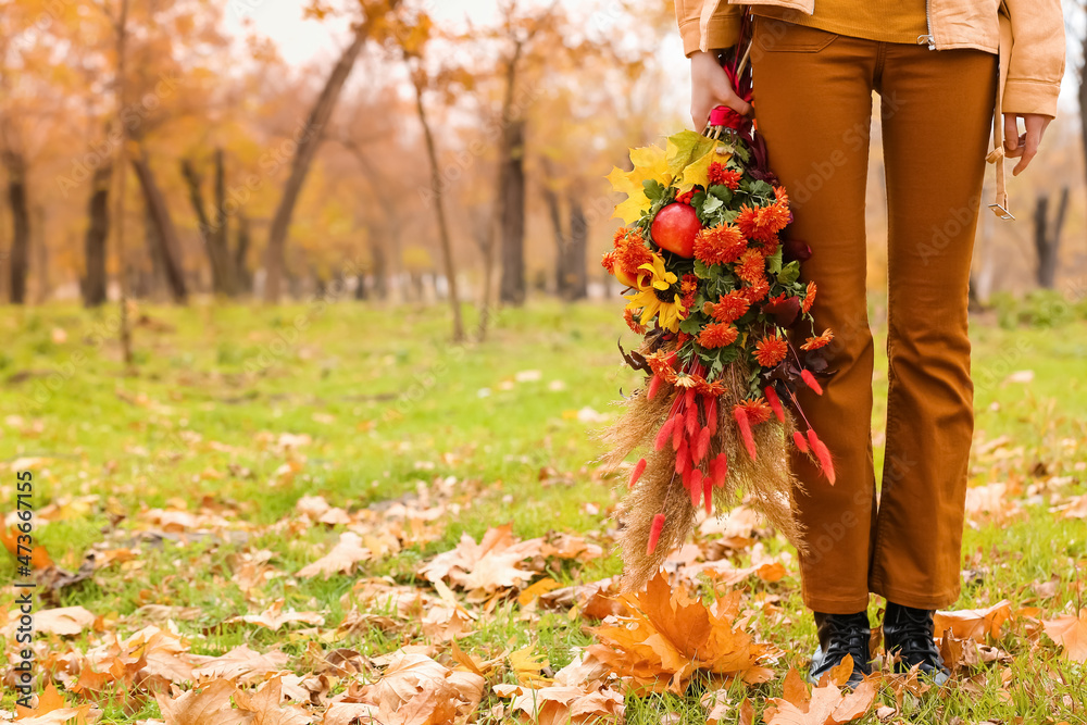 站在公园草地上，手里拿着秋天美丽花束的女人