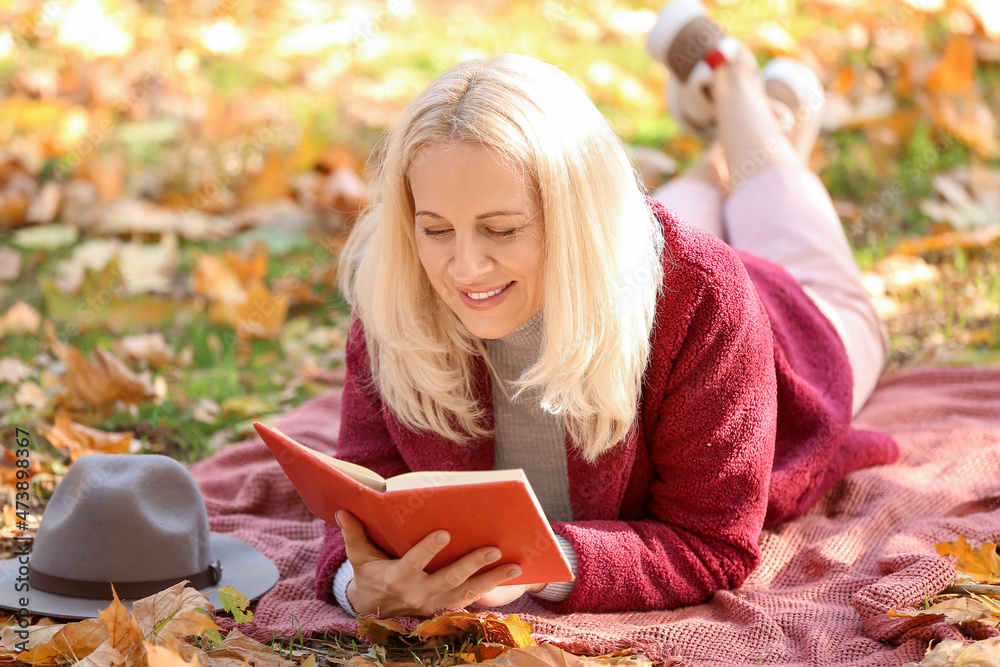成熟的女人在秋季公园看书
