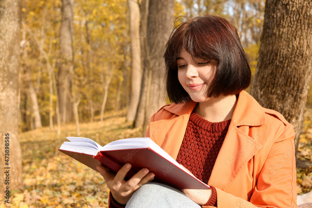 Beautiful woman reading interesting book in autumn park on sunny day
