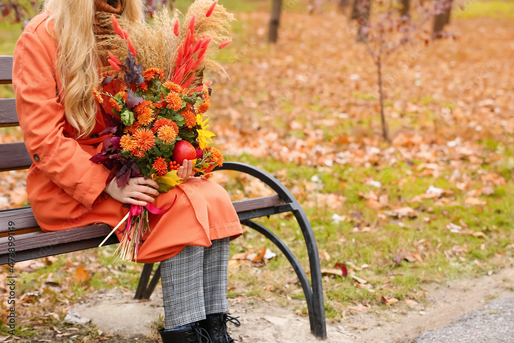 秋天公园里坐在长椅上捧着花束的年轻时尚女性