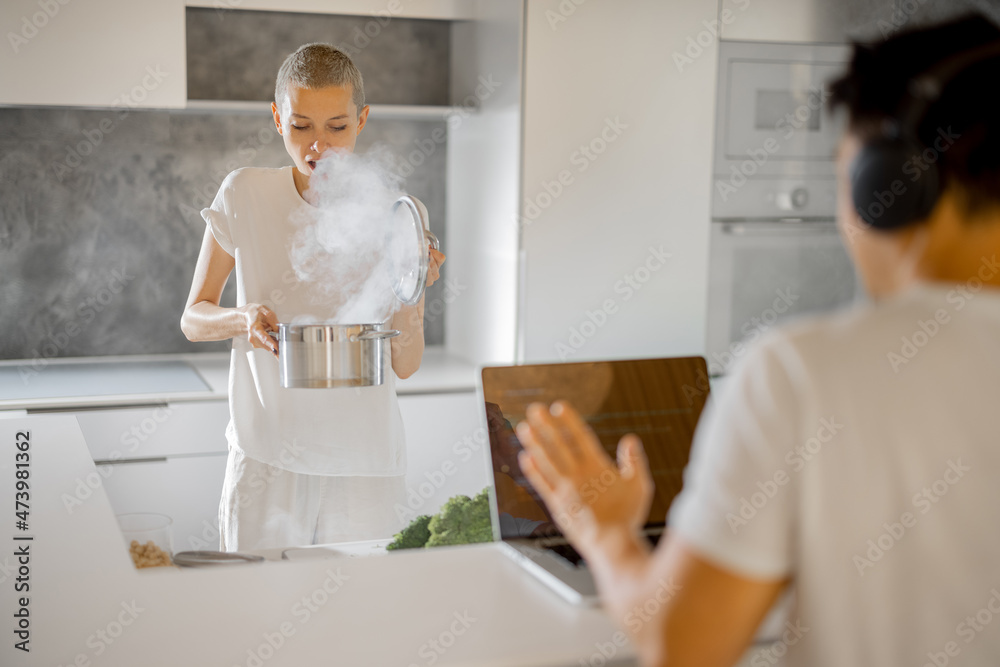 高加索妇女匆忙做饭，而她的丈夫戴着耳机在笔记本电脑上工作。厨房烟雾弥漫