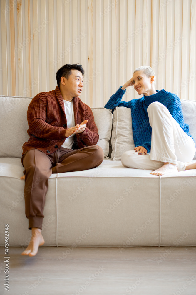 亚洲男人和欧洲女孩坐在家里的沙发上聊天。关系和消费的概念