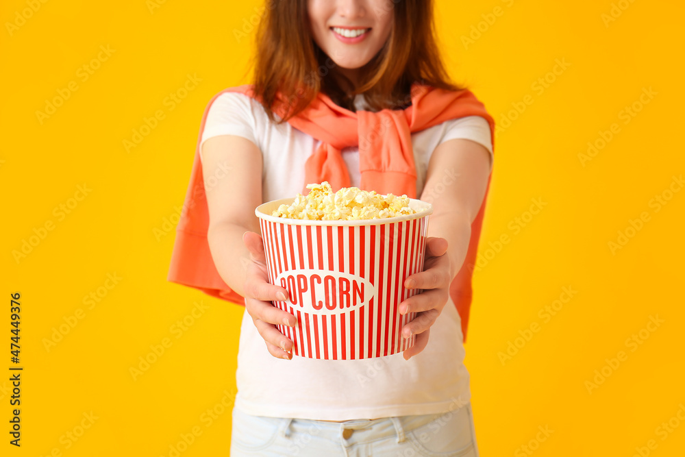 Young Asian woman with bucket of tasty popcorn on yellow background