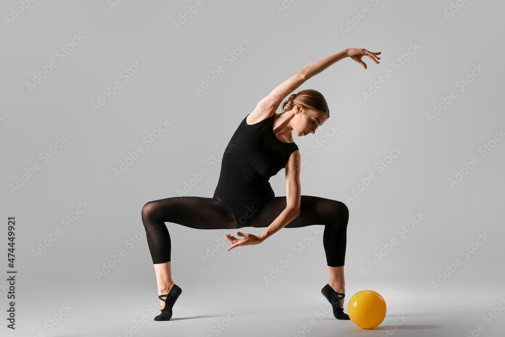 漂亮的年轻女子用灰色背景的球做体操