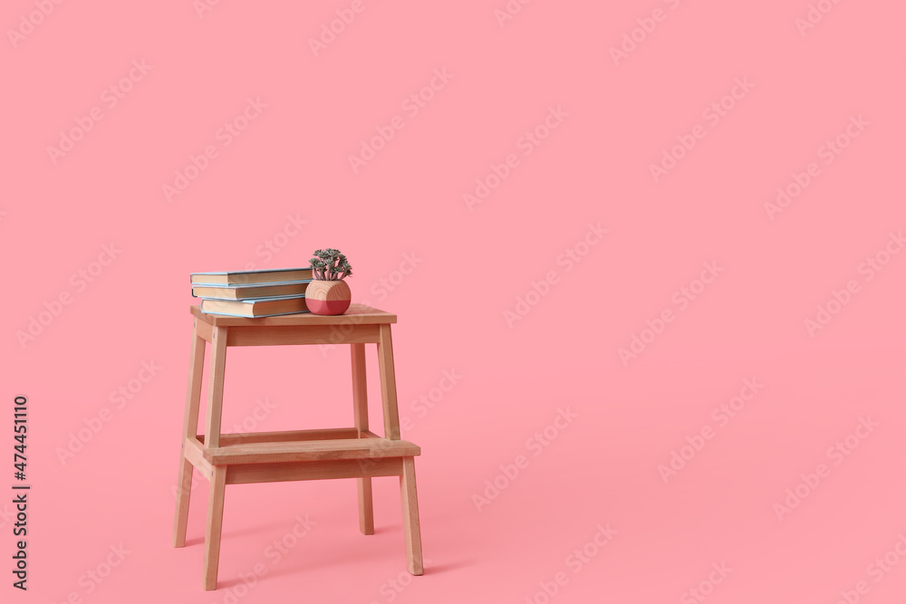 粉红色背景上有书籍和室内植物的木制台阶凳