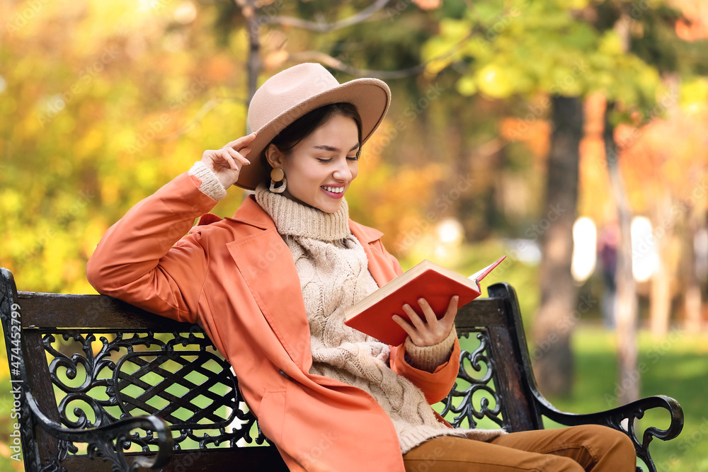 美丽微笑的女人在公园的长椅上读有趣的书