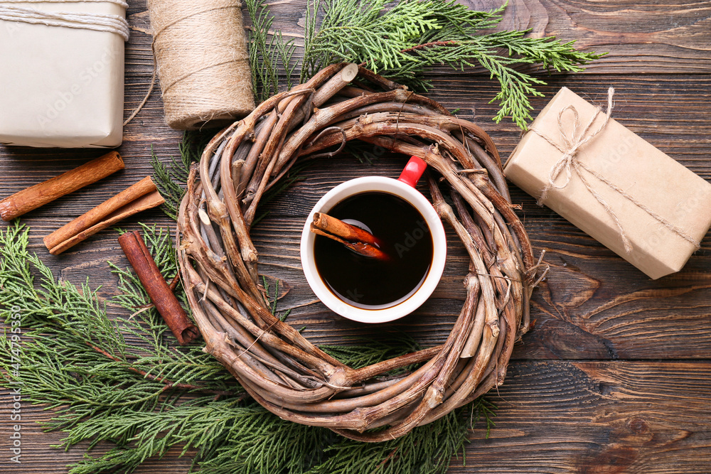 Cup of tasty coffee with cinnamon, fir branches and wreath on wooden background