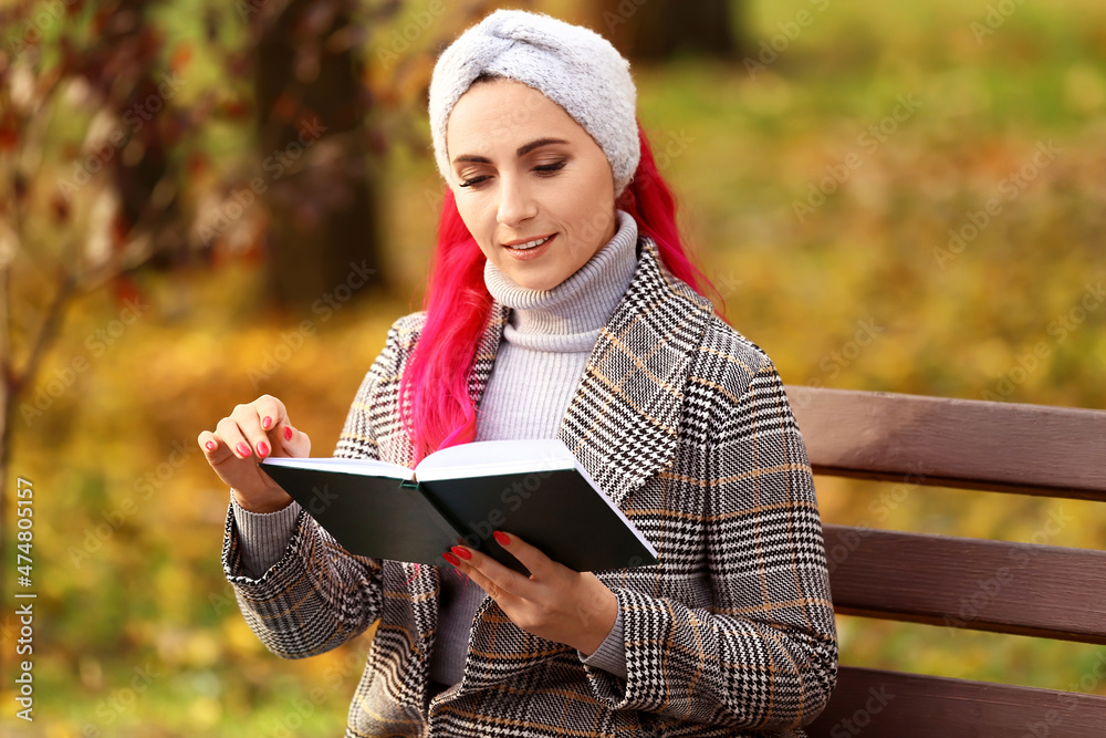 美丽的女人在秋天公园的长椅上看书