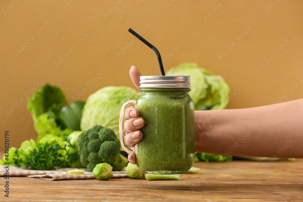 Female hand with mason jar of healthy green smoothie and vegetables on wooden background