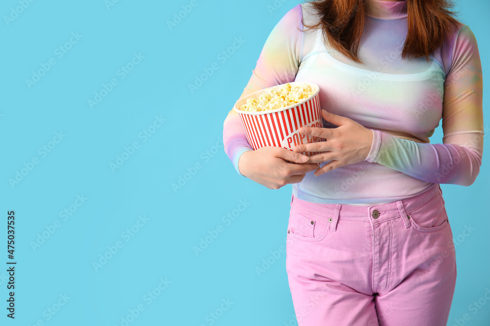 时尚的年轻女性，蓝色背景下有一桶美味的爆米花