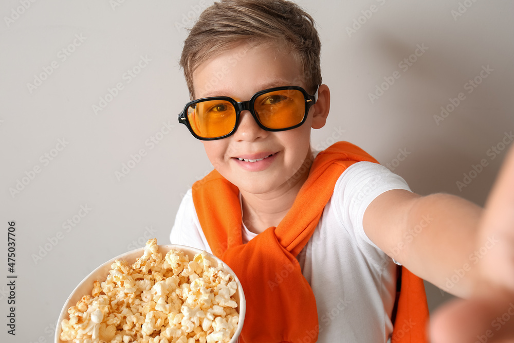 戴眼镜的小男孩拿着一桶美味的爆米花在浅色背景下自拍