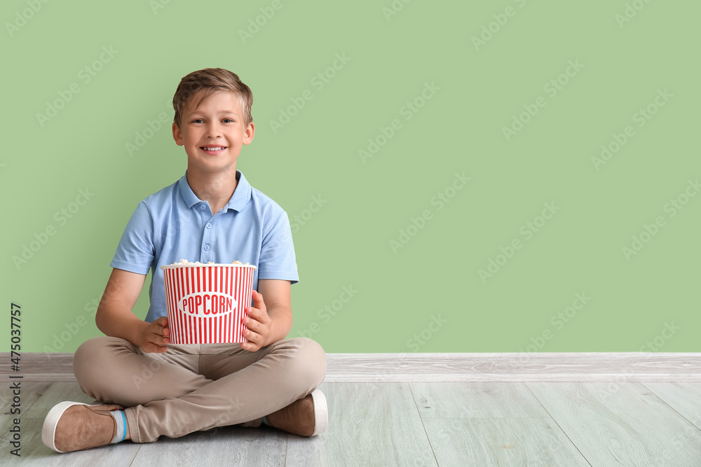 小男孩拿着一桶美味的爆米花坐在绿墙附近