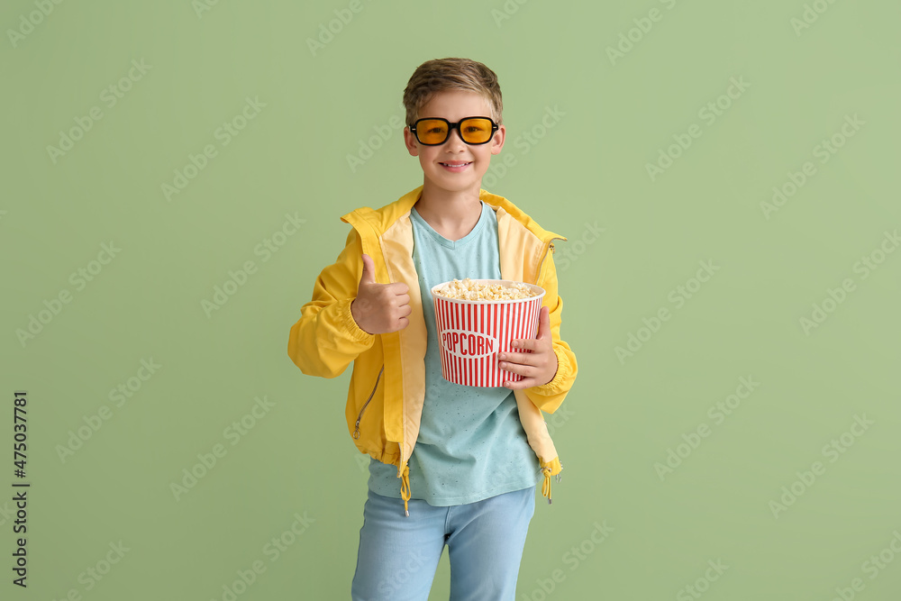 戴眼镜的小男孩，绿色背景下有一桶美味的爆米花