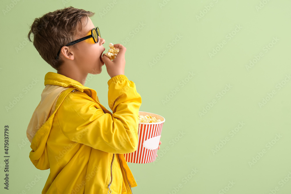 戴眼镜的小男孩在绿色背景下吃美味的爆米花