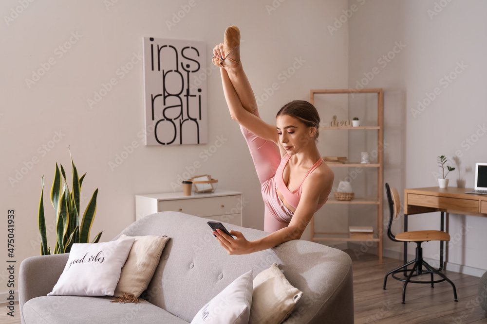 Beautiful young woman with phone doing gymnastics at home